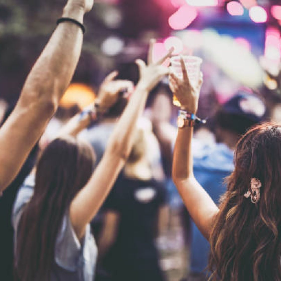 Rear view of carefree people having fun while listening music on a festival with their arms raised.