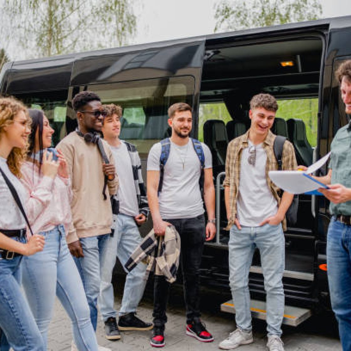 Group of students getting on a minibus for a field trip. The teacher is holding a clipboard and doing a headcount